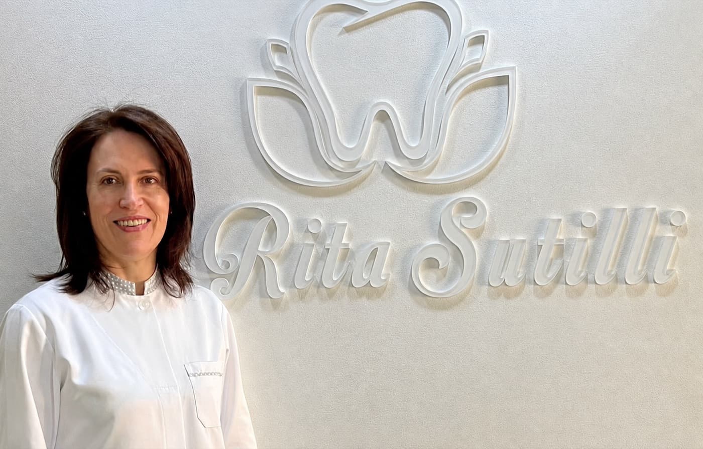 Dra. Rita Sutilli no consultório, ao lado do letreiro com sua marca